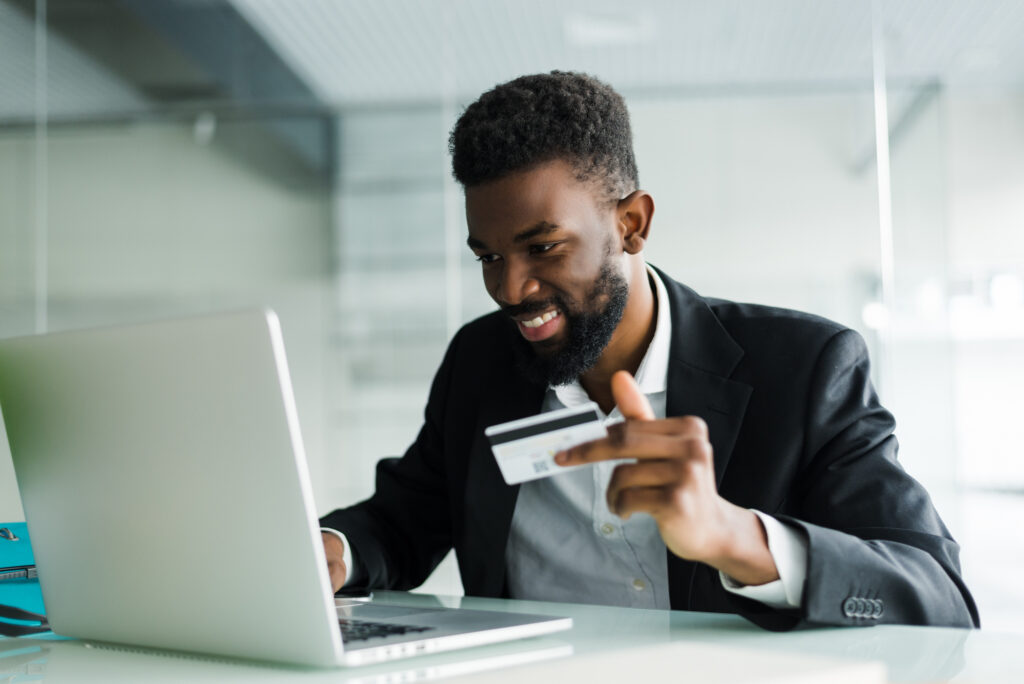 Smiling man holding credit card while working in front of laptop