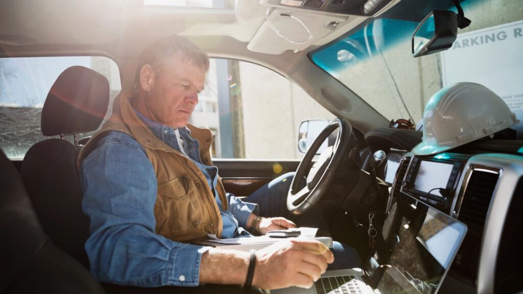 Worker in truck doing paperwork while looking at his laptop